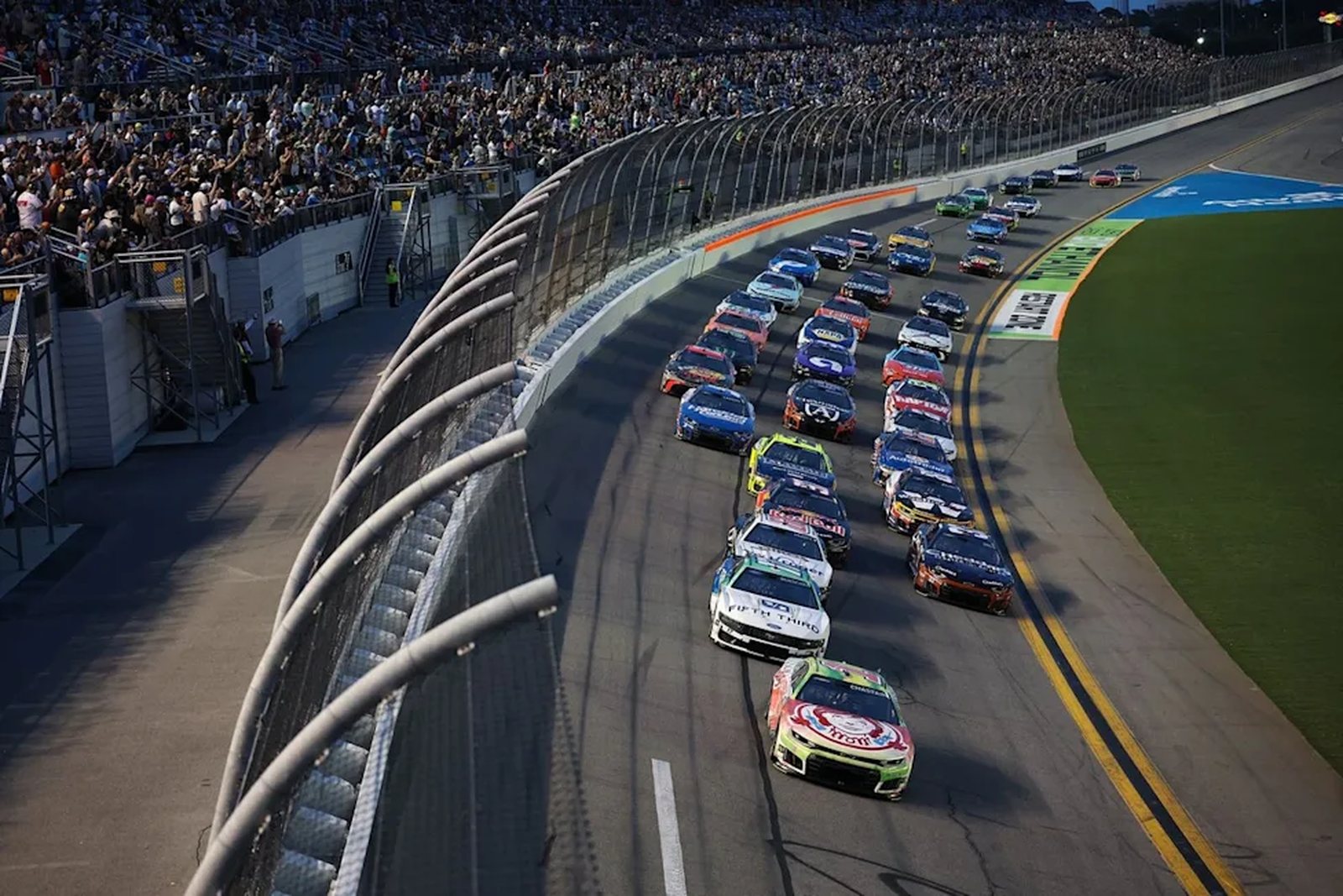 A full field of NASCAR cars running under the lights